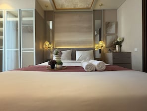 A hotel room with a large bed, bedside lamps, a dresser, and a mirror. - Luxe Elegant 2Br At Apartment The Rosebay (Surabaya)