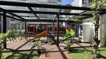 Un espacio exterior techado con un parque infantil, un refrigerador y un árbol.