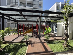 A covered outdoor area with a playground, a refrigerator, and a tree. - Luxe Elegant 2Br At Apartment The Rosebay (Surabaya)