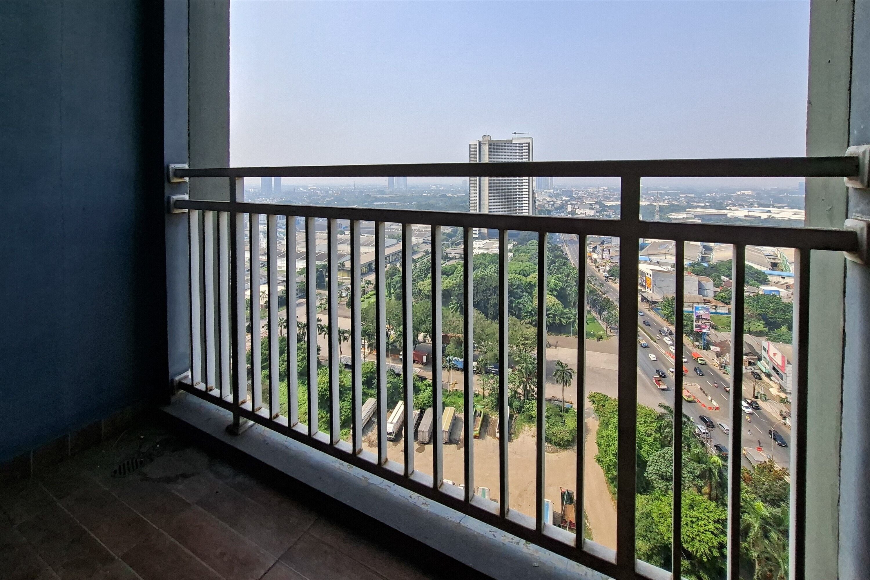 A balcony with a metal railing overlooking a cityscape with buildings and greenery.