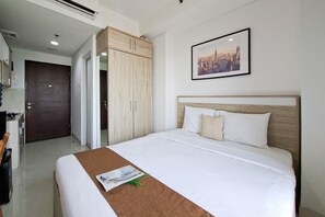 Ein Hotelzimmer mit einem Bett, einem Holzschrank, einem Stadtbild im Bilderrahmen und einer Tür zu einem anderen Raum.
