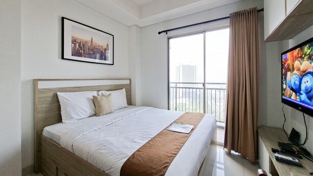 A hotel room with a bed, a television, a window with curtains, and a framed picture on the wall. - Bright Comfortable Studio Room At Apartment Springwood Residence Tangerang (Tangerang)