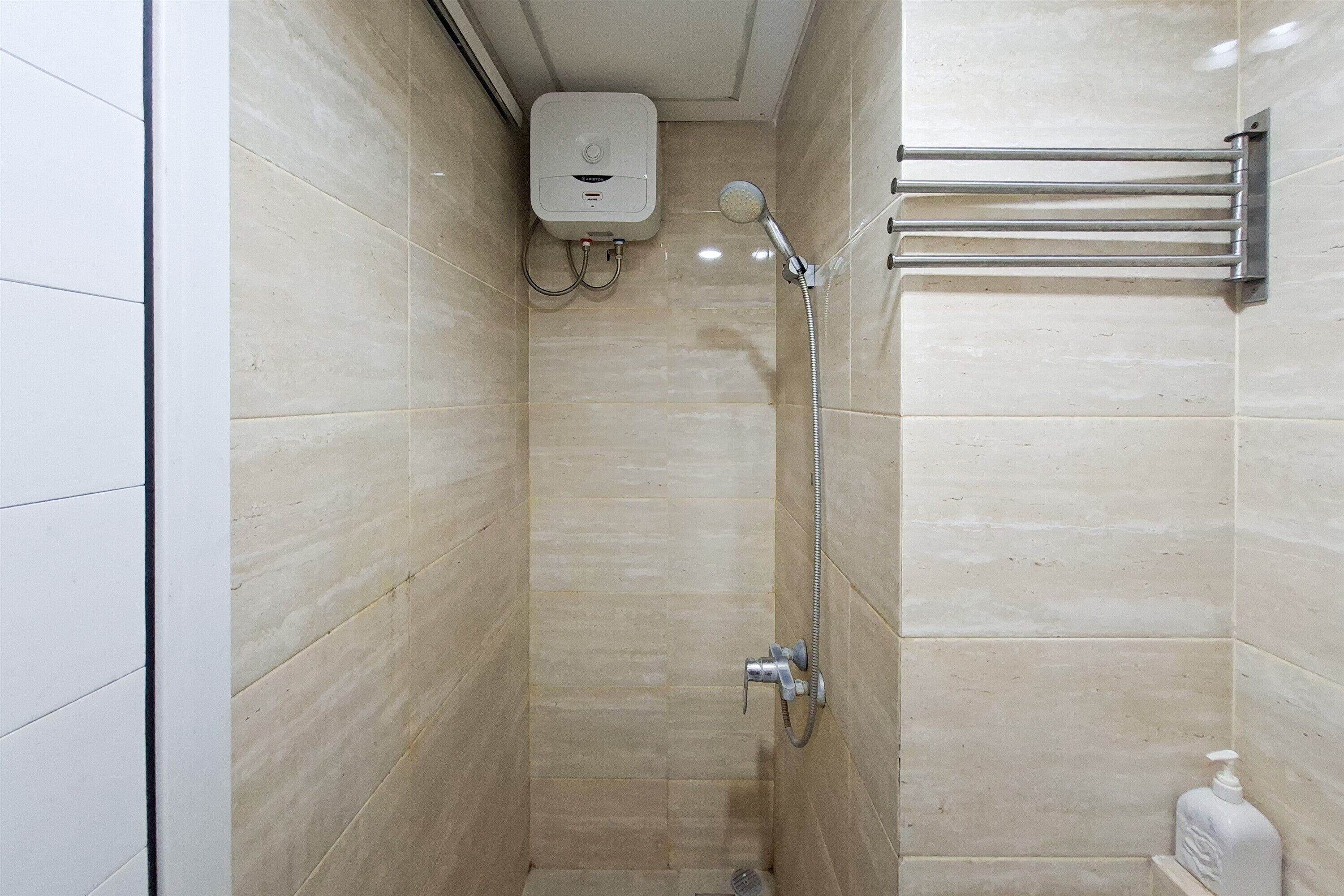 Un petit espace de douche carrelé, équipé d’un pommeau de douche à main, d’un robinet mural et d’un distributeur de savon.