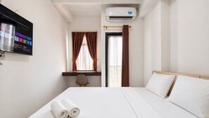 Ett hotellrum med en säng, ett skrivbord, en stol, en luftkonditioneringsanläggning och en tv.
