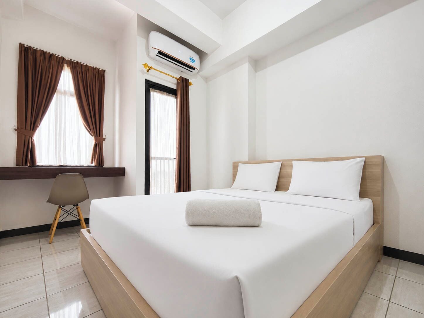 A hotel room with a bed, a desk, and an air conditioning unit.