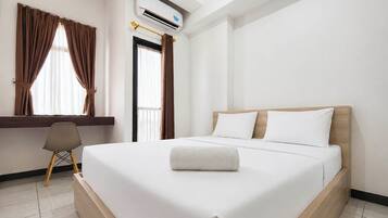 A hotel room with a bed, a desk, and an air conditioning unit.
