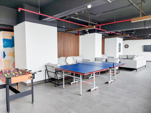A modern indoor space with a foosball table, ping pong table, and sofas.