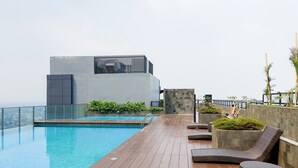A rooftop pool area with a modern building, lounge chairs, and a view of the city.