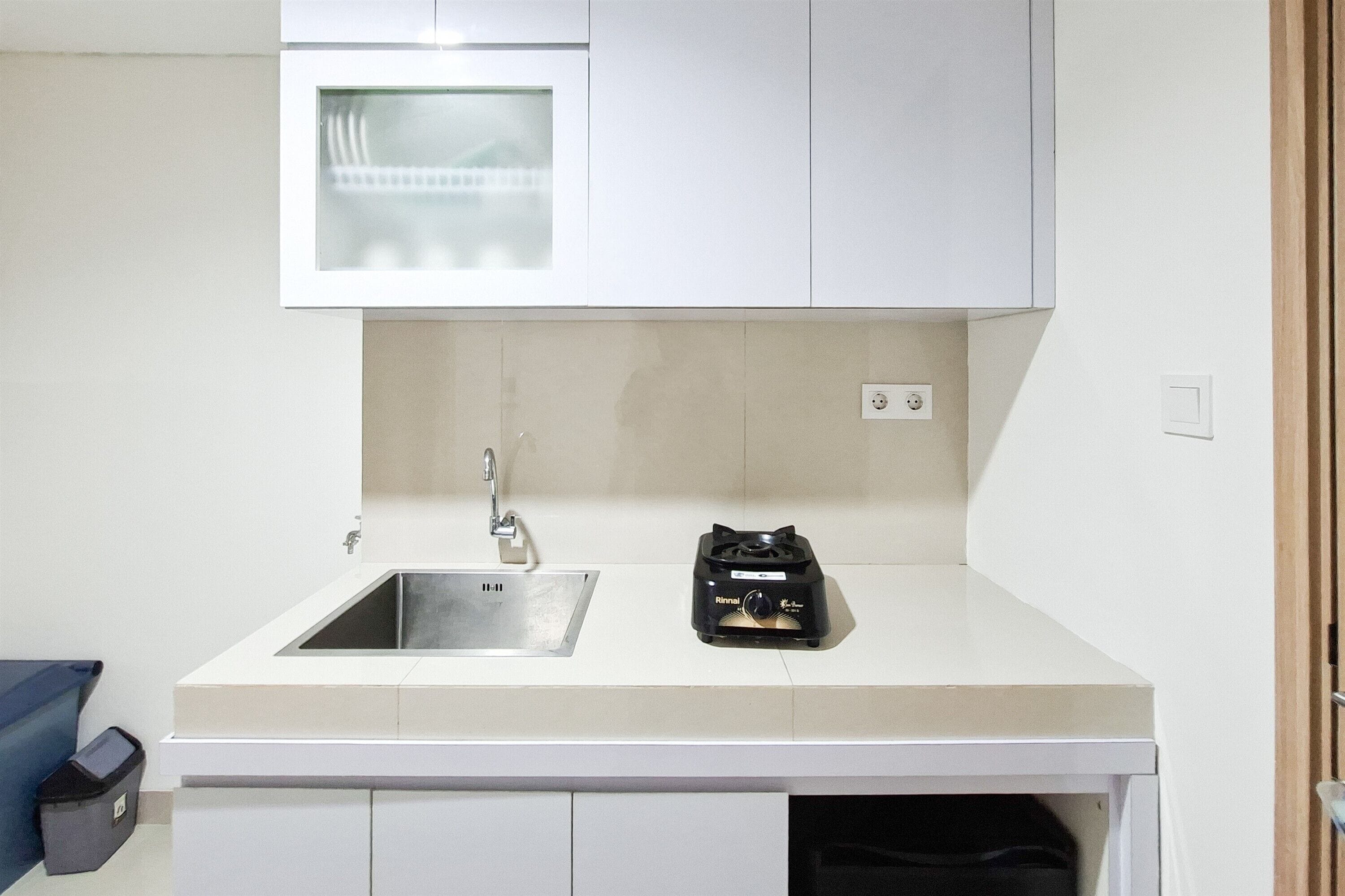 Una cocina compacta con un lavamanos de acero inoxidable, un pequeño electrodoméstico negro en la encimera y un microondas sobre el lavamanos.