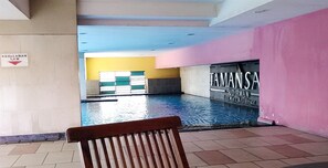 Ein Schwimmbeckenbereich mit einer Bank im Vordergrund, einem Schild, das eine Wassertiefe von 1,4 Metern angibt, und einer Wand mit den Aufschriften 'TAMAN SA' und 'SUDIRMAN Executive Residence'.
