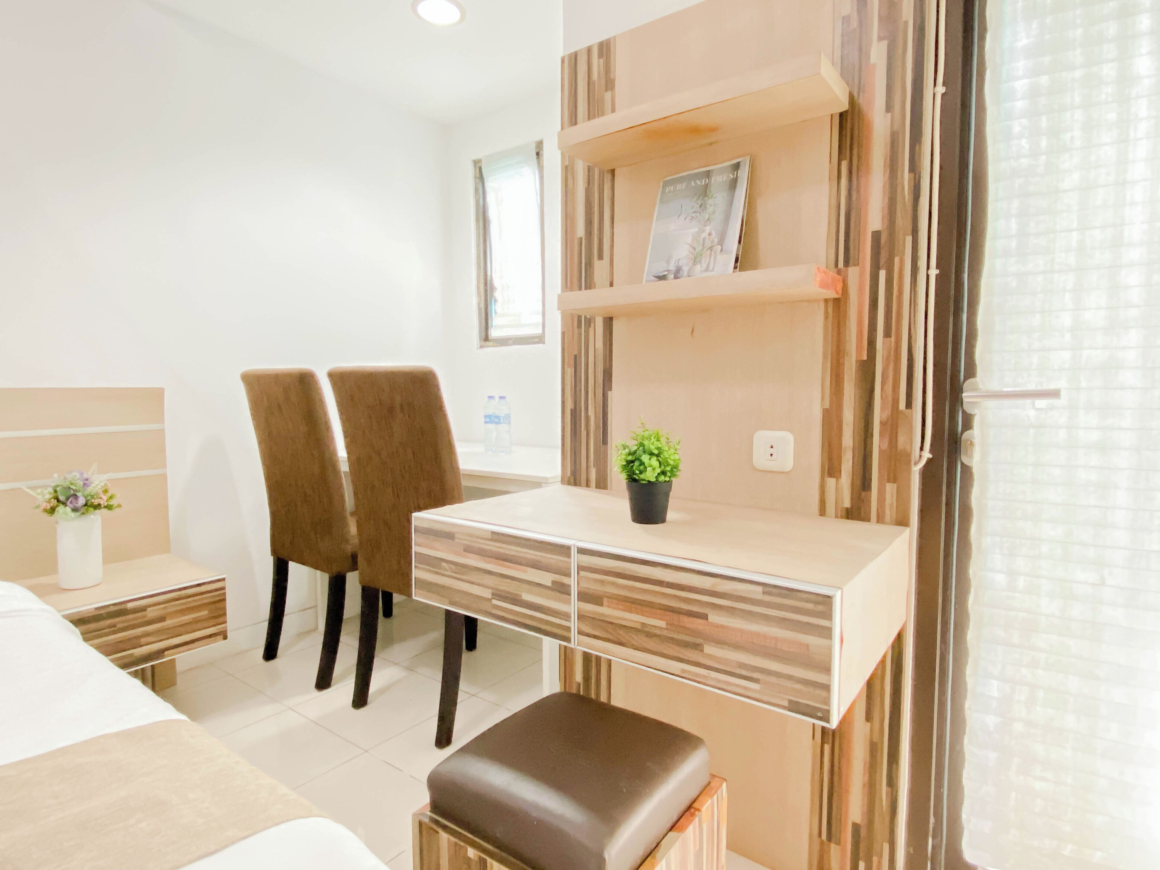 Habitación de hotel con cama, escritorio, silla, planta en maceta y estante con un cuadro.