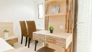 Habitación de hotel con cama, escritorio, silla, planta en maceta y estante con un cuadro.