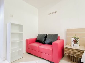 Ein Zimmer mit einem roten Sofa, einer weißen Regaleinrichtung und einem Holznachttisch mit einer Zeitschrift.