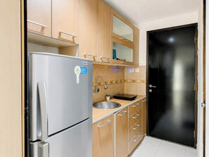 Eine kompakte Küche mit Edelstahl-Kühlschrank, Holzschränken, einer schwarzen Tür und einer kleinen Arbeitsfläche mit Spüle.