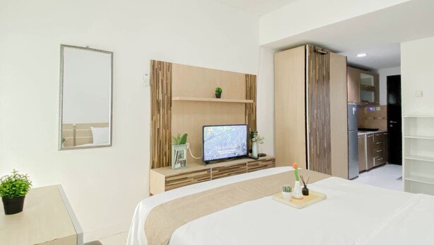 Moderni hotellihuone, jossa on sänky, televisio, työpöytä ja pieni keittiönurkkaus.