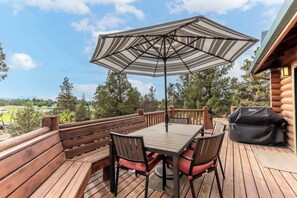En træterrasse med et bord, stole og en stribet parasol.