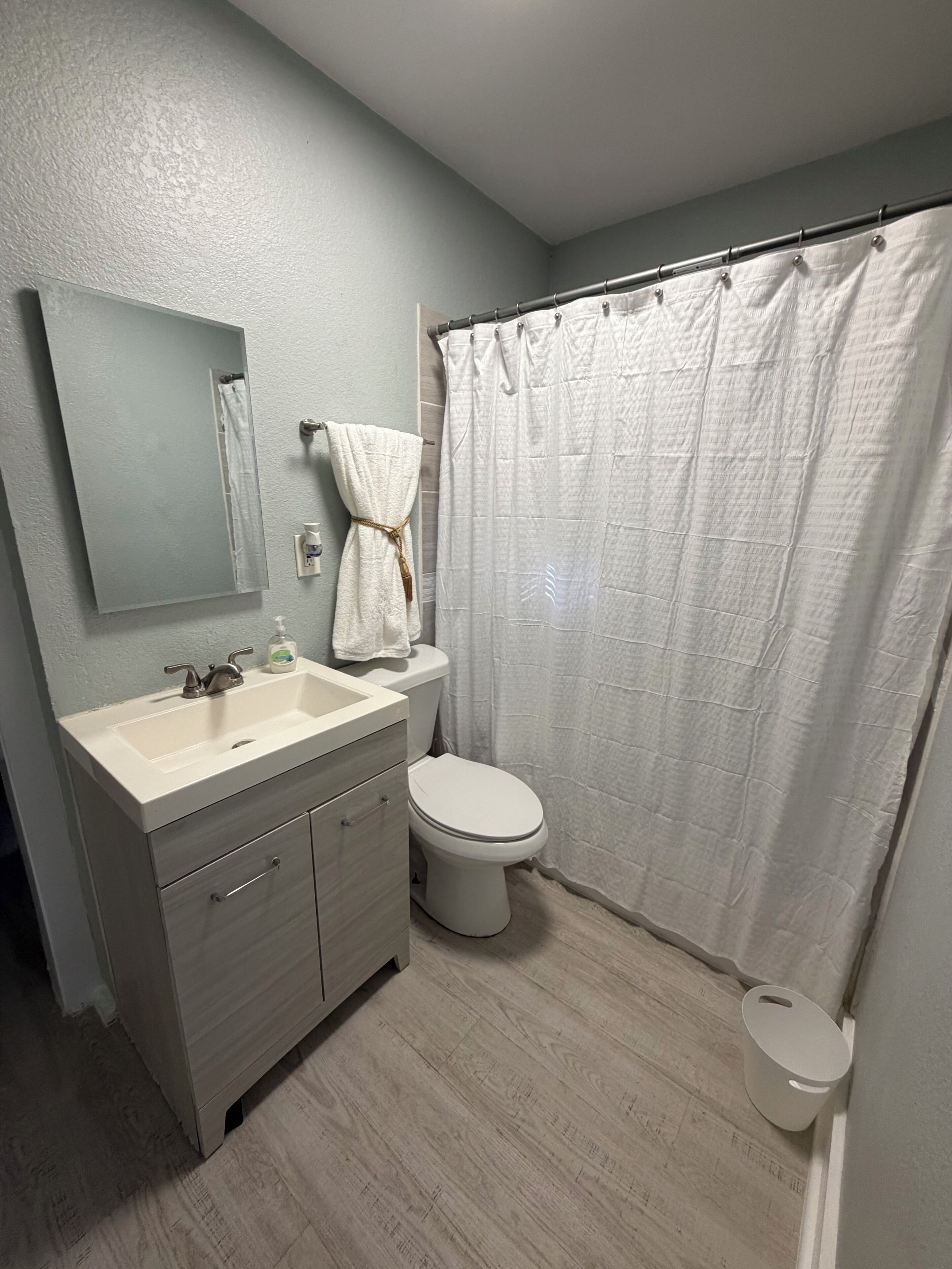 Ein Badezimmer mit Waschbecken, Spiegel, Toilette und Duschvorhang.