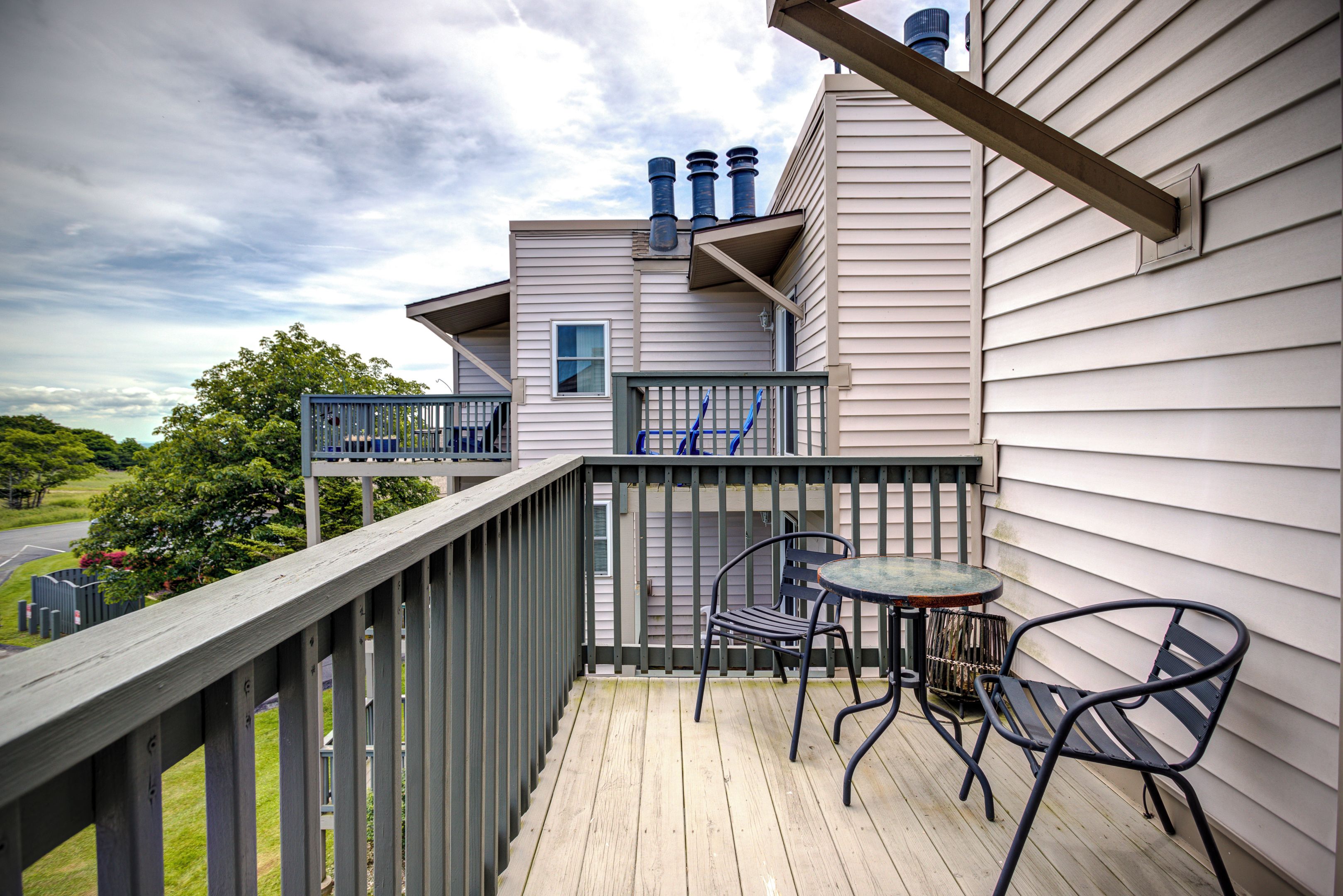 A wooden deck with outdoor furniture, a view of a road, and a building with a window and vents.