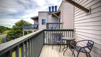 A wooden deck with outdoor furniture, a view of a road, and a building with a window and vents.