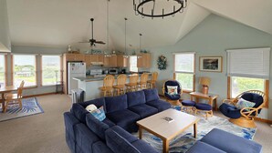 A spacious living area with a sectional sofa, a coffee table, and a dining area with wooden chairs. - 7853 - Anchor Management Spacious 6BR, 5.2BA oceanside home in Frisco for up to 12 guests. (Frisco)