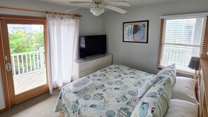 A bedroom with a bed, a television, a ceiling fan, a window with blinds, and a balcony door. - 7853 - Anchor Management Spacious 6BR, 5.2BA oceanside home in Frisco for up to 12 guests. (Frisco)