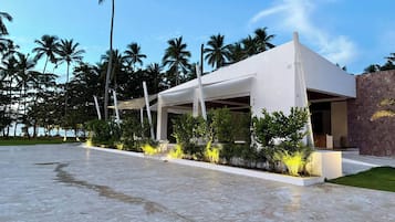 A modern building with a flat roof, surrounded by palm trees and a paved area.