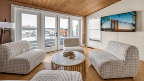 A modern living room with a checkered sofa set, a round coffee table, and a large window with a city view. - Rooftop | Fire pit | Luxury | Sleeps 10 | (Cincinnati)