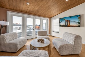 Ein modernes Wohnzimmer mit einer karierten Couchgarnitur, einem runden Couchtisch und einem großen Fenster mit Blick auf die Stadt.