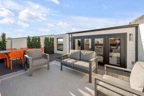 Eine Dachterrasse mit Sitzgelegenheiten im Freien, einer Couch und einer Glasschiebetür zu einem Innenbereich.