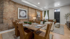 A dining area with a brick wall, a dining table set for four, and a living area with a sofa and a TV. - Rooftop | Fire pit | Luxury | Sleeps 10 | (Cincinnati)