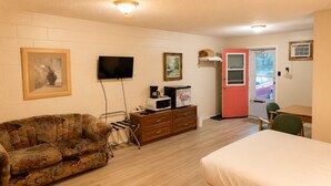 Una habitación con sofá, televisión, microondas, cafetera, una puerta y una ventana.