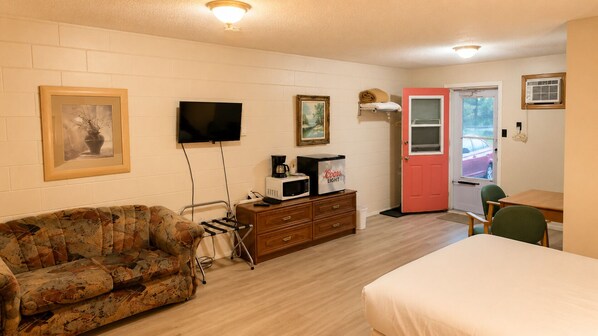 A room with a sofa, a television, a microwave, a coffee maker, a door, and a window.