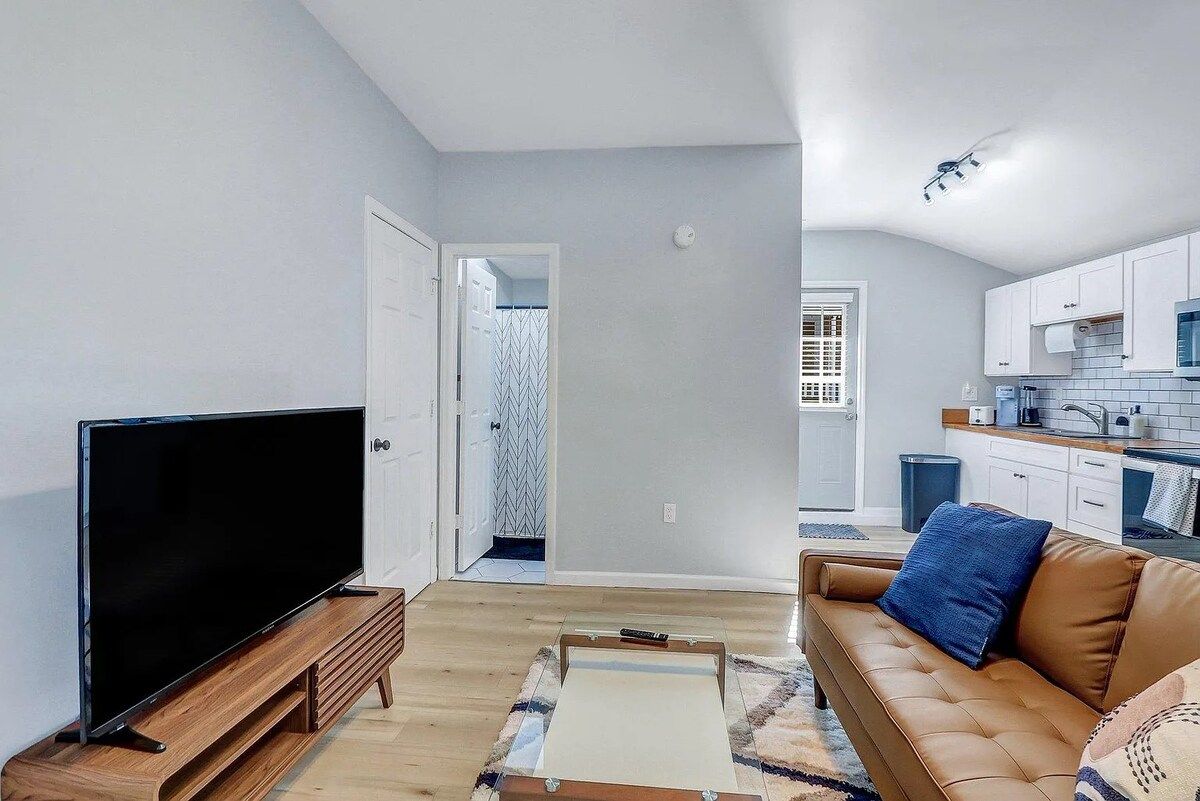 A living room with a flat-screen TV on a wooden stand, a brown leather sofa, and a patterned rug.