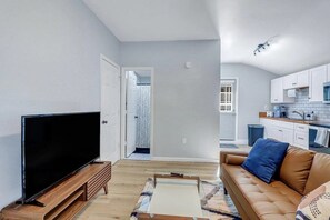 A living room with a flat-screen TV on a wooden stand, a brown leather sofa, and a patterned rug. - 2bd/1ba Cottage * Renovated * Dogs Welcome (Savannah)