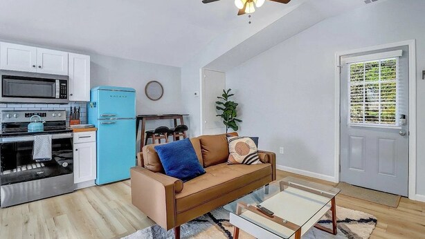 Um espaço de estar compacto com cozinha compacta, geladeira azul, sofá marrom e ventilador de teto.