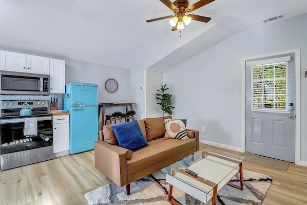 A compact living space with a kitchenette, a blue refrigerator, a brown sofa, and a ceiling fan. - 2bd/1ba Cottage * Renovated * Dogs Welcome (Savannah)