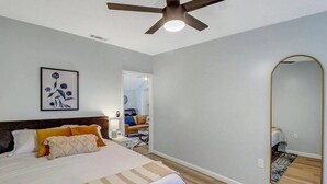 Quarto com cama, ventilador de teto, espelho grande e pintura na parede.