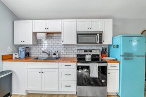 A kitchen with white cabinets, a microwave, a stove, and a blue refrigerator. - 2bd/1ba Cottage * Renovated * Dogs Welcome (Savannah)
