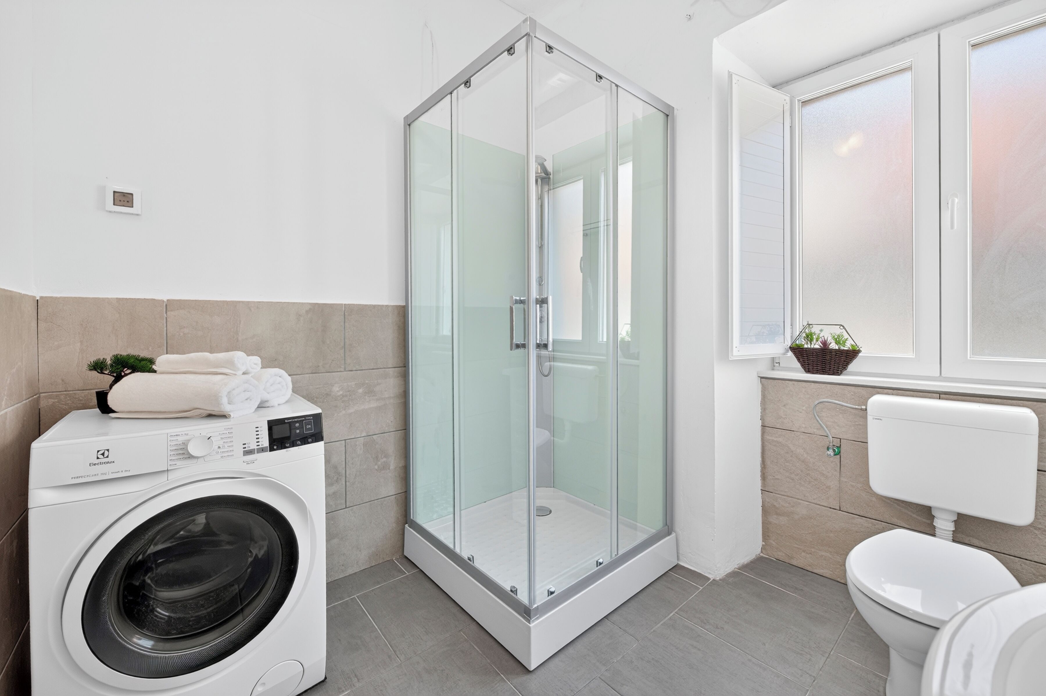 A modern bathroom with a glass-enclosed shower, a washing machine, and a toilet.