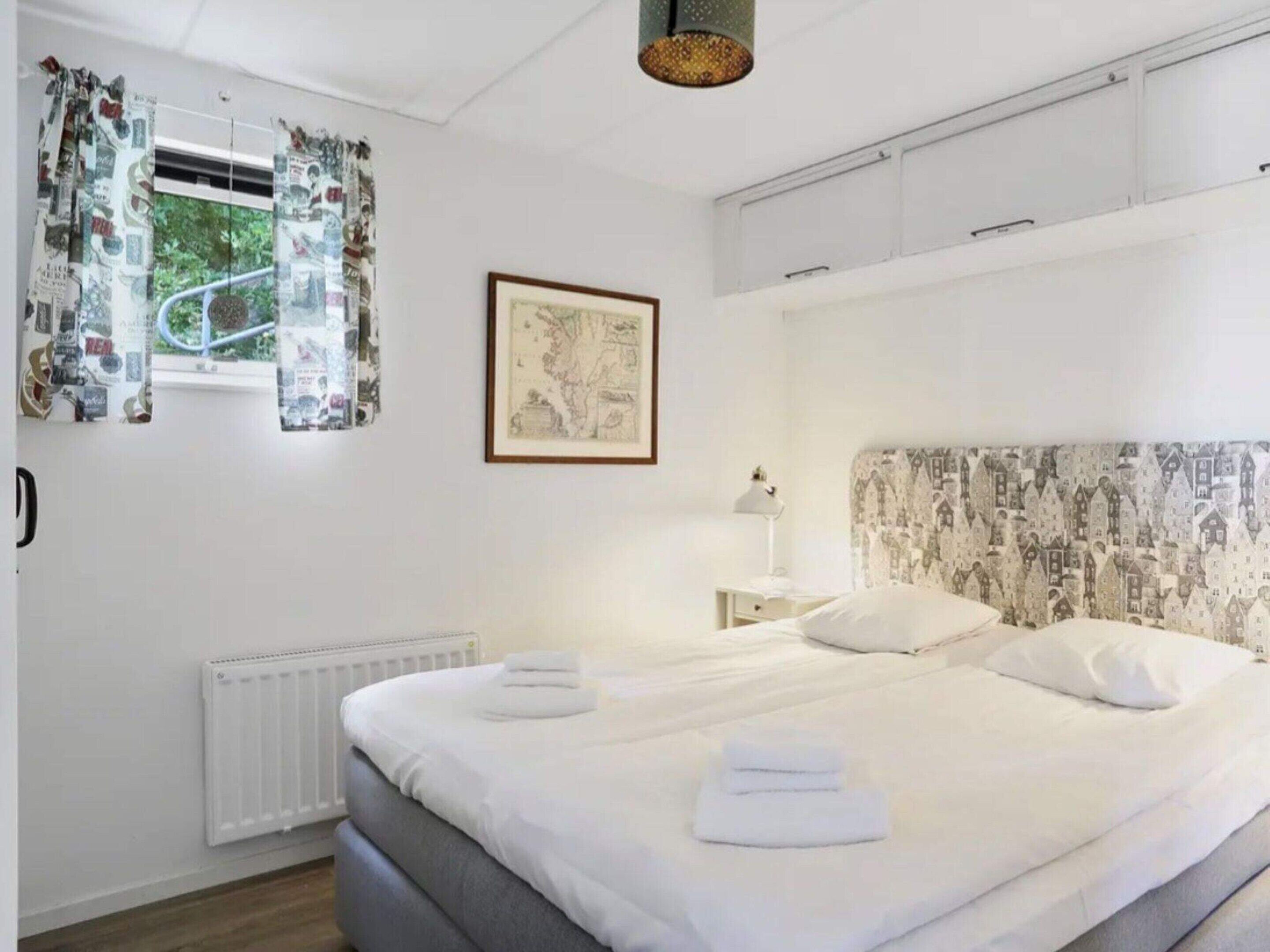 Une chambre à coucher comprenant un lit, un radiateur, une fenêtre avec des rideaux, un tableau encadré et une tête de lit à motifs.