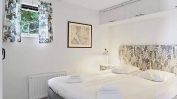 A bedroom with a bed, a radiator, a window with curtains, a framed picture, and a headboard with a pattern.