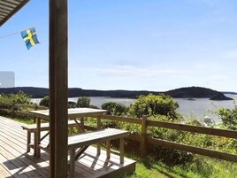 Terraza de madera con mesas de picnic con vistas a un lago y colinas.