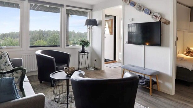 A modern living room with a sofa, armchairs, a coffee table, a TV, and a view of the outdoors. - 5 Star Holiday Home in Uddevalla (Uddevalla)