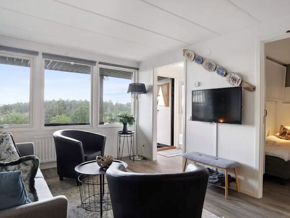 Una sala de estar moderna con sofá, sillones, una mesita de centro, televisor y vistas al exterior.