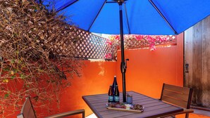 Un patio al aire libre con una mesa, sillas y un paraguas azul.