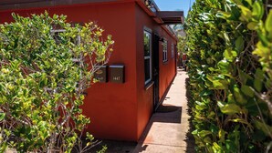 Un edificio rojo con dos números de puerta visibles, 649 y 1647, y un sendero bordeado de follaje verde.
