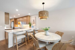 A modern kitchen with wooden cabinets, a stainless steel refrigerator, and a round dining table with wicker chairs. - Martinique South 506 (Holmes Beach)