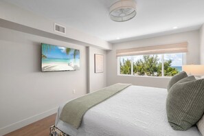 Een slaapkamer met een groot bed, een raam met uitzicht op groen en een schilderij van een strand.