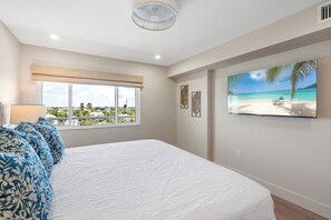 Quarto com uma cama grande, janela com vista para a praia e uma pintura com cena de praia.