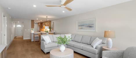 A modern living room with a grey sectional sofa, a round coffee table with a plant, a ceiling fan, and recessed lighting.